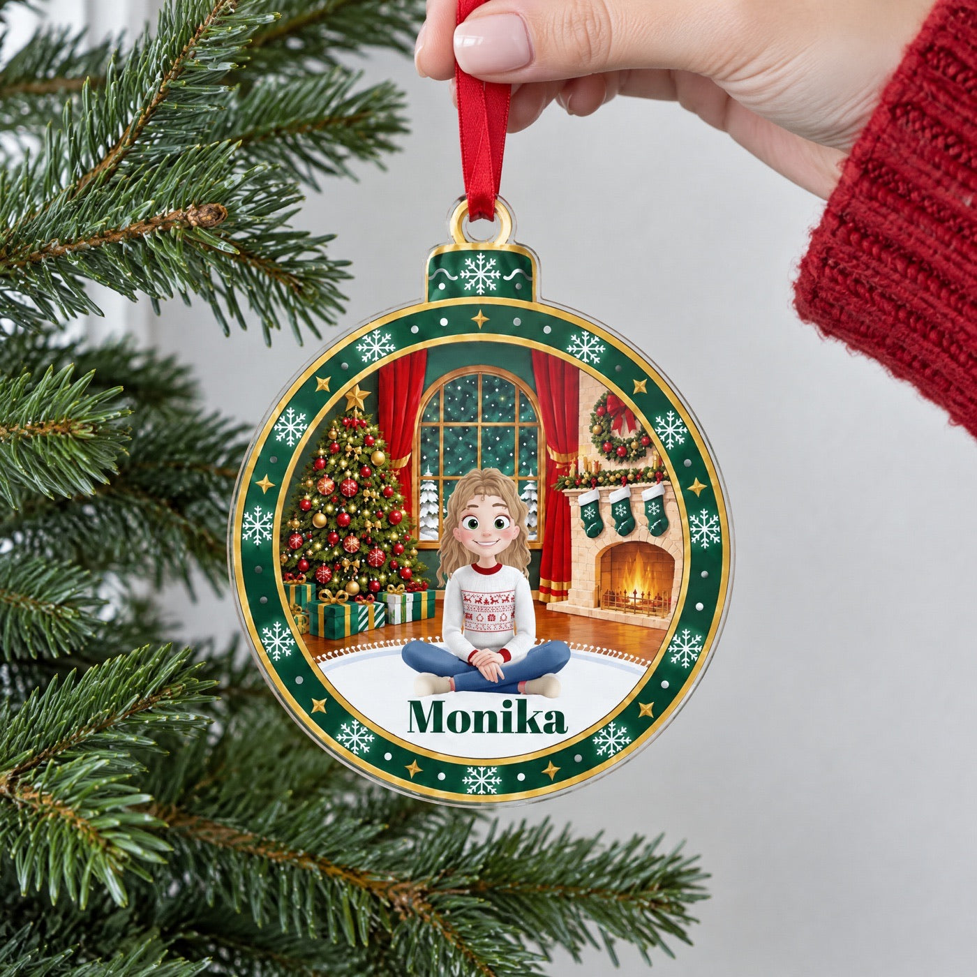 Ruka drží vánoční ozdobu se jménem Monika u větve smrku